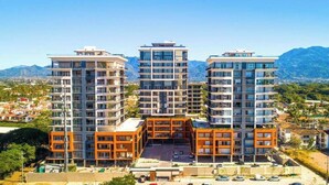 Un moderno complejo de apartamentos con varios edificios de gran altura, un patio central y montañas al fondo.