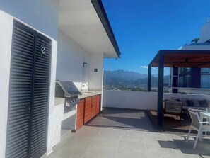 A modern outdoor kitchen with a grill, wooden cabinets, and a view of mountains.