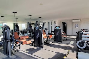 A gym with various exercise machines, mirrors, and orange chairs.
