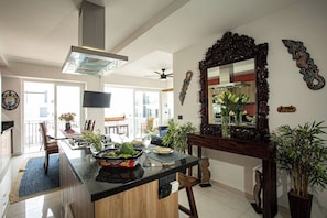 A modern kitchen with a central island, a large mirror, and various plants.