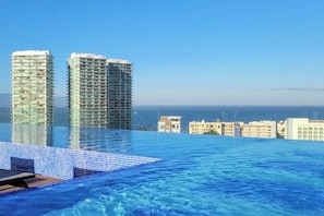 A hotel pool with a view of two tall buildings and the ocean.