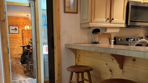 A kitchen with wooden cabinets, a stainless steel microwave, and two wooden stools.