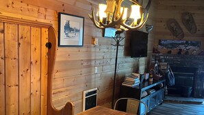 A wooden dining area with a chandelier, wooden walls, a fireplace, and a view of the outdoors.