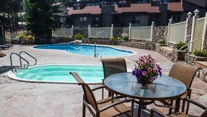 A pool area with two pools, a glass table with chairs, and a flower vase.