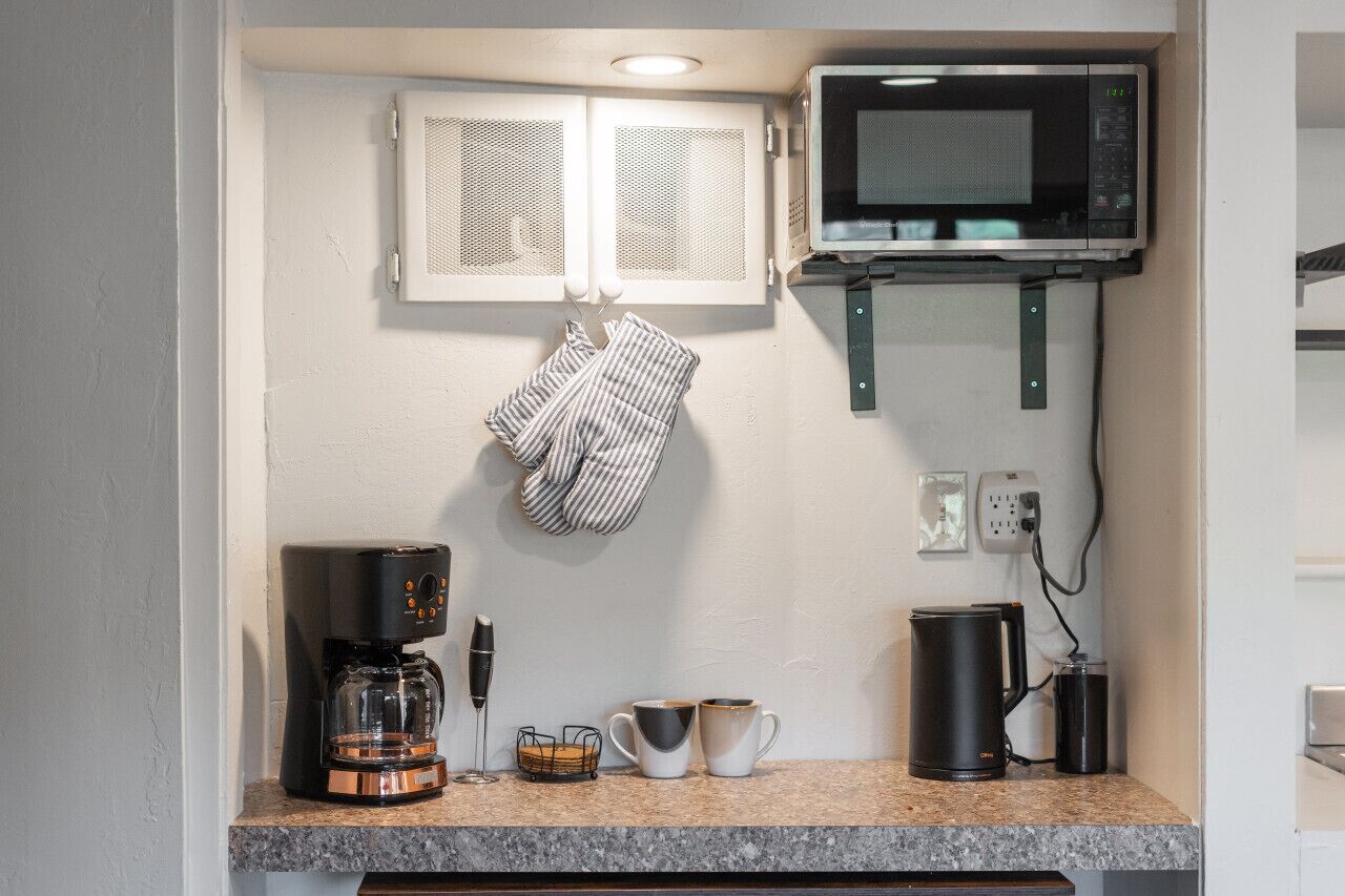 A kitchen with a coffee maker, two cups, a kettle, and a microwave.