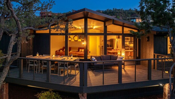 Una casa moderna con terraza de madera, amplios ventanales y un interior acogedor con comedor y zona de estar.
