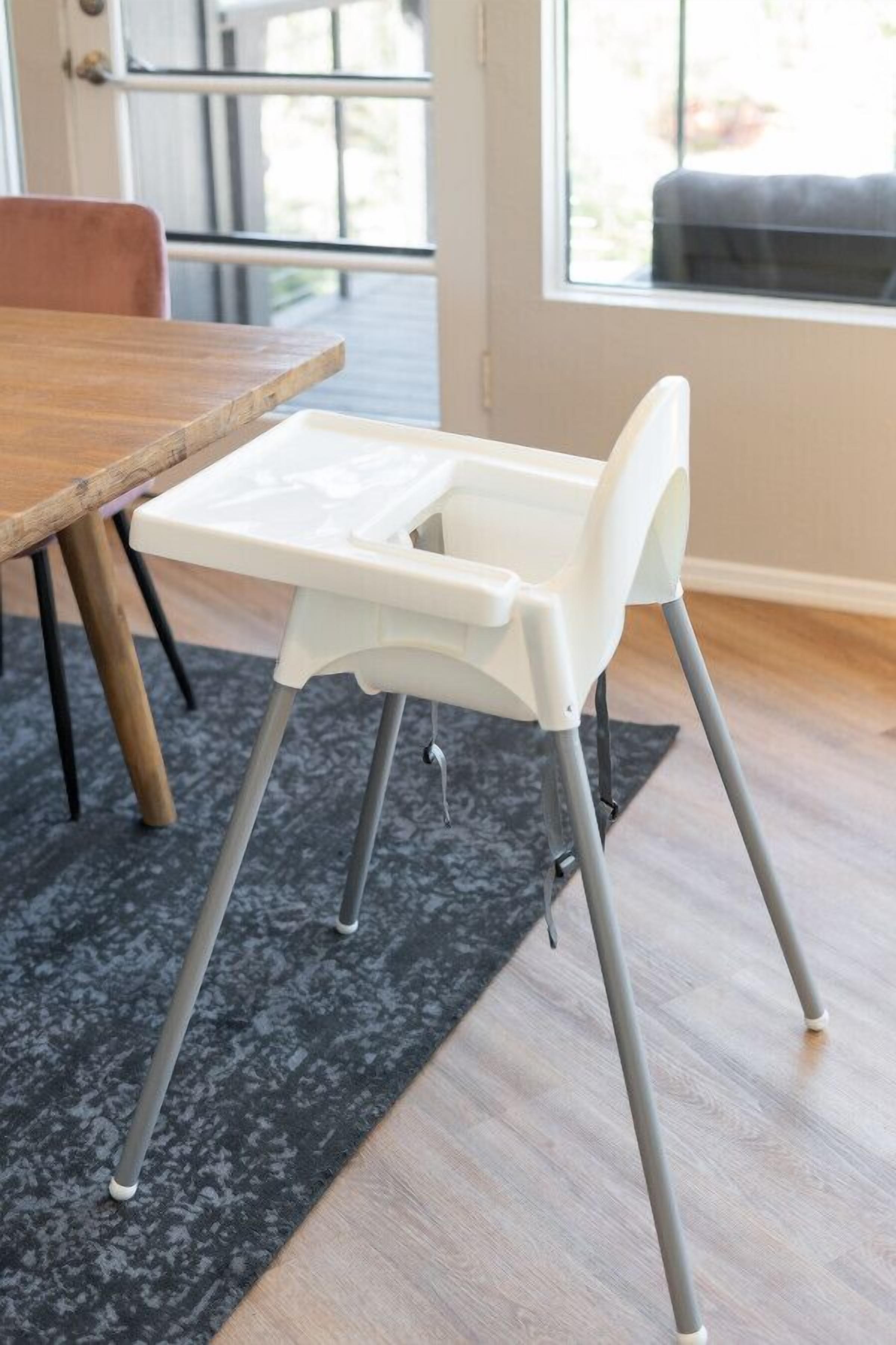 A high chair with a tray table, positioned in a room with a wooden table and a dark rug.
