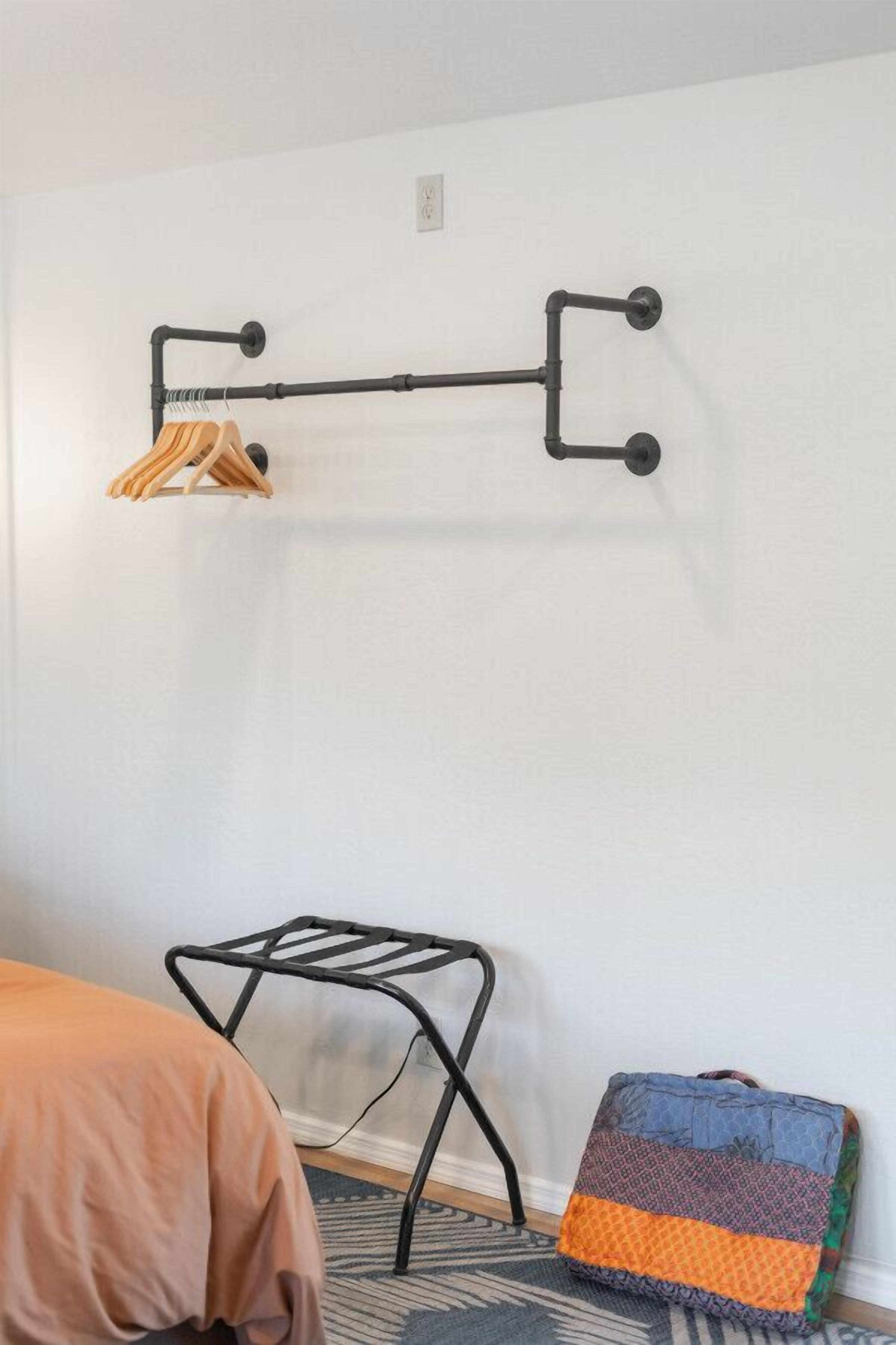 A room with a black metal rack for hanging clothes, a small black metal stool, and a colorful cushion on the floor.