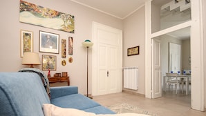 Una sala de estar con un sofá azul, una lámpara y varias obras de arte enmarcadas en la pared.
