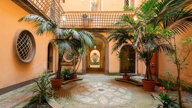 Une cour avec un sol pavé de pierres, des plantes en pot et un motif décoratif central en mosaïque.