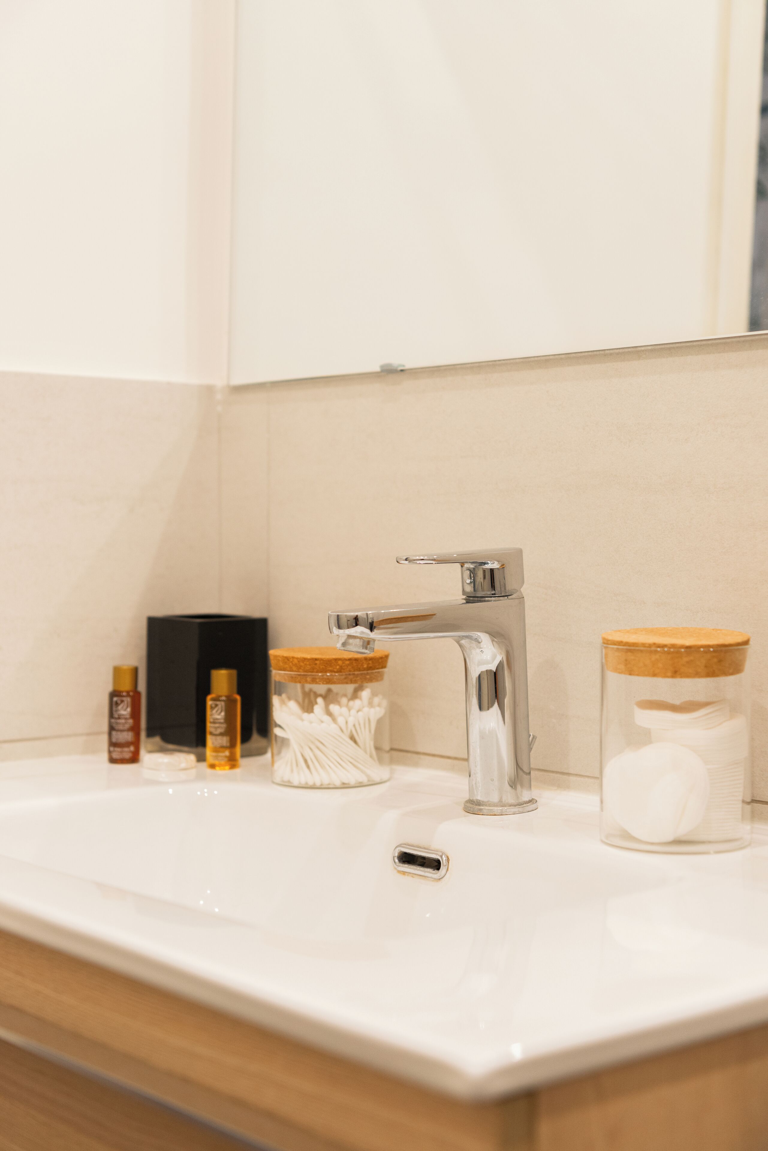 A bathroom sink with a modern faucet, a tissue dispenser, and two glass jars with cork lids.