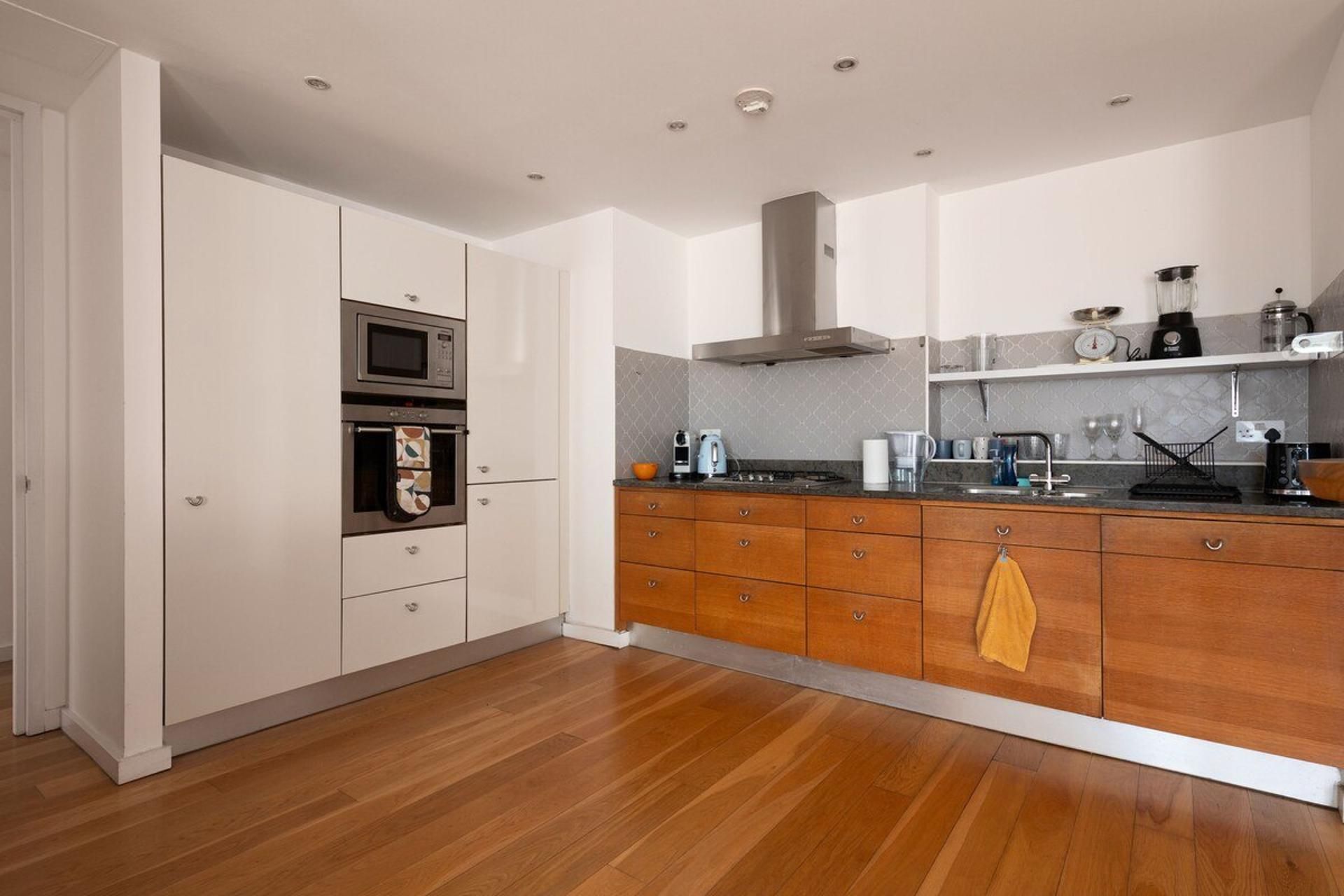 A modern kitchen with wooden cabinets, a built-in oven, and a stainless steel range hood.