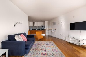 Una sala de estar moderna con un sofá, un tapete estampado, un televisor y una cocina al fondo.