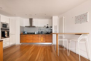 Una cocina moderna con armarios de madera, horno empotrado y una isla central con taburetes de bar.