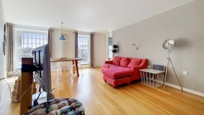 Ein geräumiges Wohnzimmer mit einem roten Sofa, einem Holzessttisch und einem Fernseher.