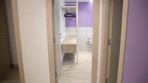Un couloir menant à une salle de bain équipée d’un rideau de douche suspendu, d’un lavabo et d’un miroir.