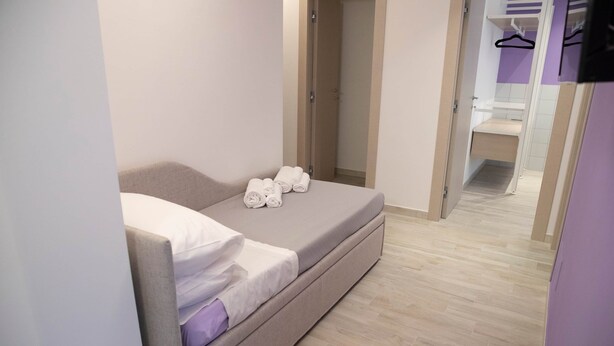 Une chambre à coucher moderne et compacte, avec un lit, des serviettes soigneusement pliées et un dressing doté d’un miroir et d’étagères.