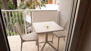Un balcon avec une table blanche et deux chaises, une petite bougie jaune et une vue sur la verdure et les bâtiments.