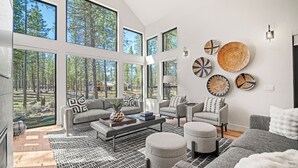 Una sala de estar amplia con ventanas grandes, chimenea y vistas al bosque.