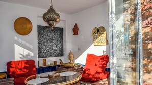Una habitación con una mesa redonda de vidrio, sillas con cojines rojos, un farol colgante y decoración en la pared.