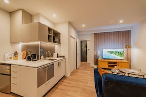 Una cucina moderna con forno a microonde integrato, macchina del caffè e frigorifero. C'è una zona pranzo con un divano blu e una TV a parete.