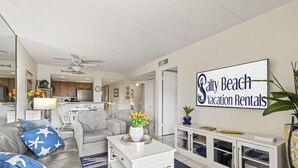 Een moderne woonkamer met een grijze bank, een salontafel en een bordje dat bevestigd is aan de muur voor Salty Beach Vacation Rentals.