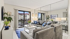 Een moderne woonkamer met een zithoek, een salontafel en een eethoek. Er is een balkon met uitzicht op het gebouw en de lucht.