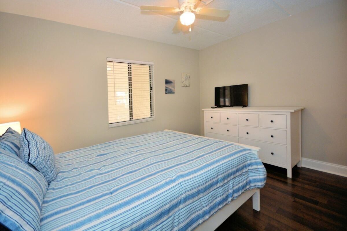 Quarto com cama, cômoda, televisão e ventilador de teto.