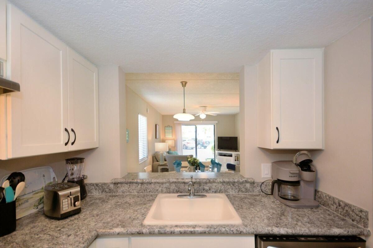 A kitchen with a granite countertop, white cabinets, a built-in sink, a coffee maker, and a ceiling fan.
