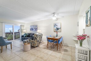 A spacious living area with a balcony, a dining table with chairs, a sofa, and a ceiling fan.