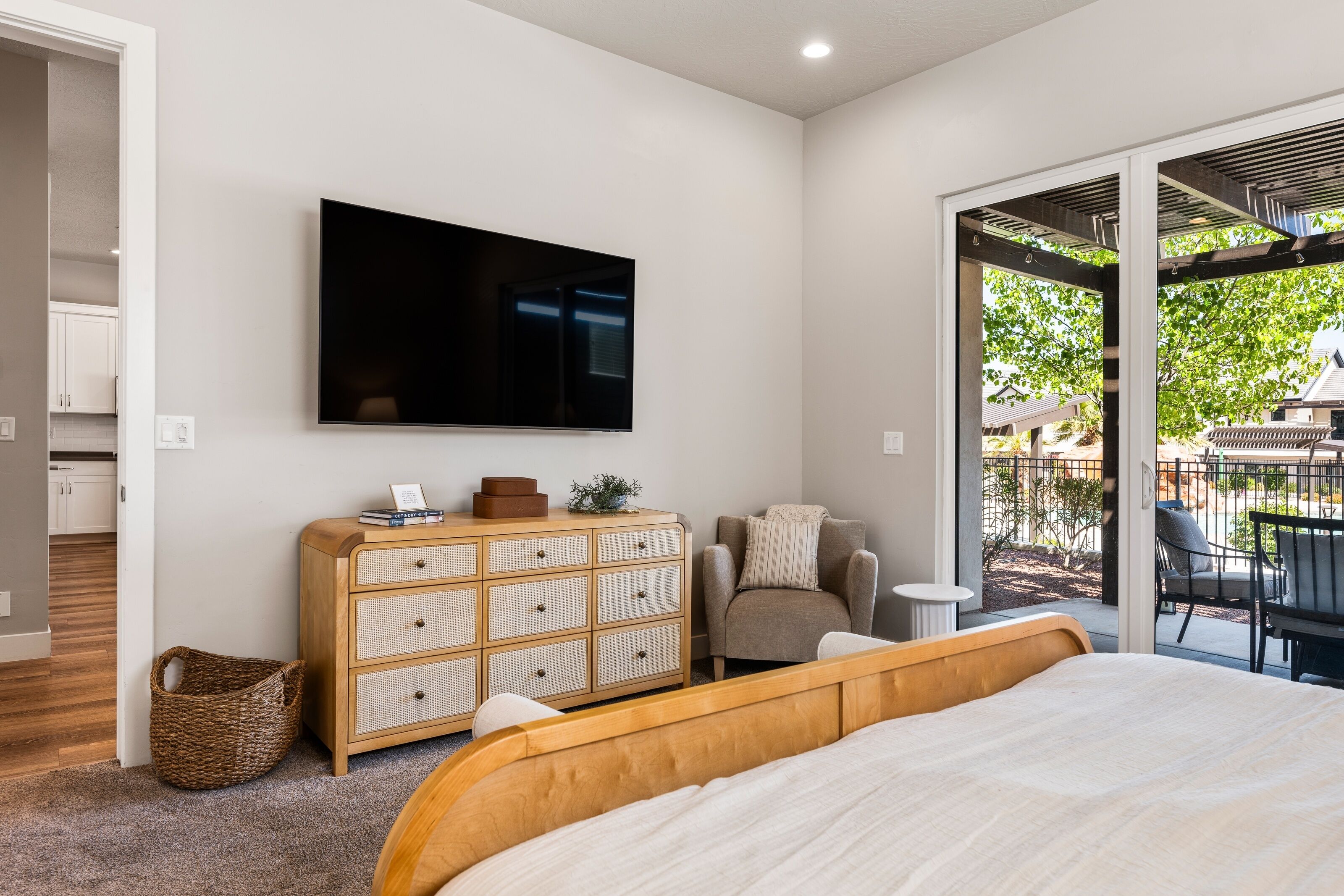 Une chambre avec un grand lit, un téléviseur fixé au mur, une commode en bois, une chaise et une vue sur l’extérieur.