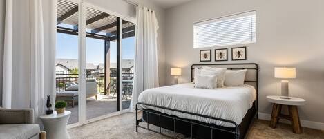 Une chambre à coucher avec un lit, deux lampes de chevet, une petite table ronde, une chaise et une vue sur l’extérieur grâce à une porte-fenêtre coulissante.