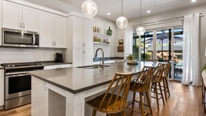 A modern kitchen with white cabinetry, a stainless steel microwave, and an island with bar stools. - Grand Slam Getaway #5 5 Bedroom Townhouse (Santa Clara)