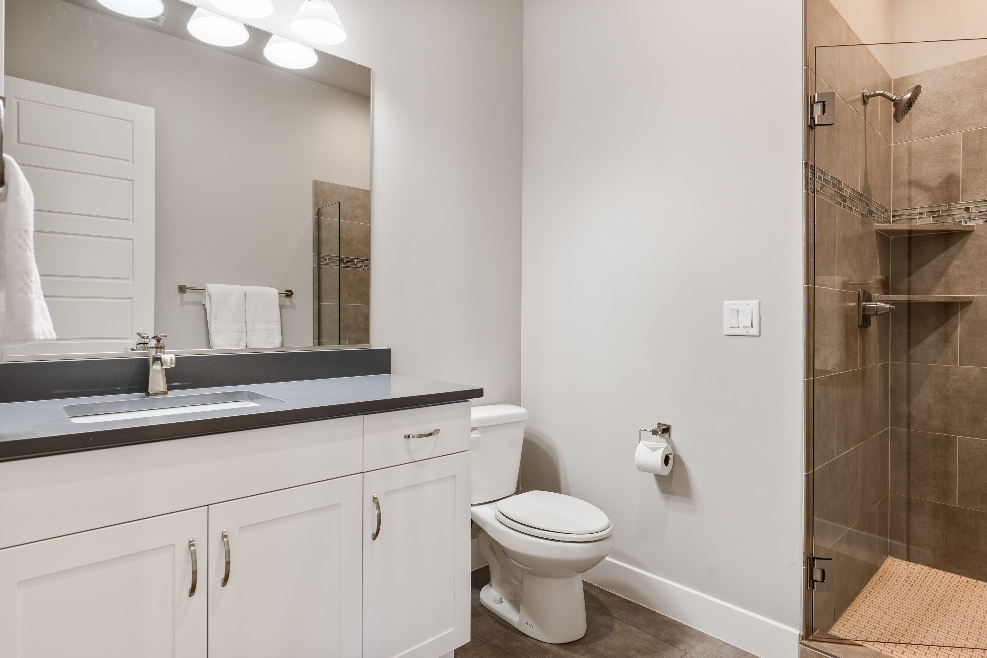 A modern bathroom with a white sink, mirror, and toilet, a glass shower enclosure, and a small rug on the floor.
