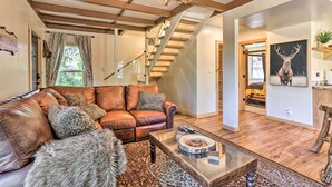A spacious living room with a leather sofa, a coffee table, and a chandelier. - Modern Big Bear Lake Cabin w/ Lake Access! (Big Bear Lake)