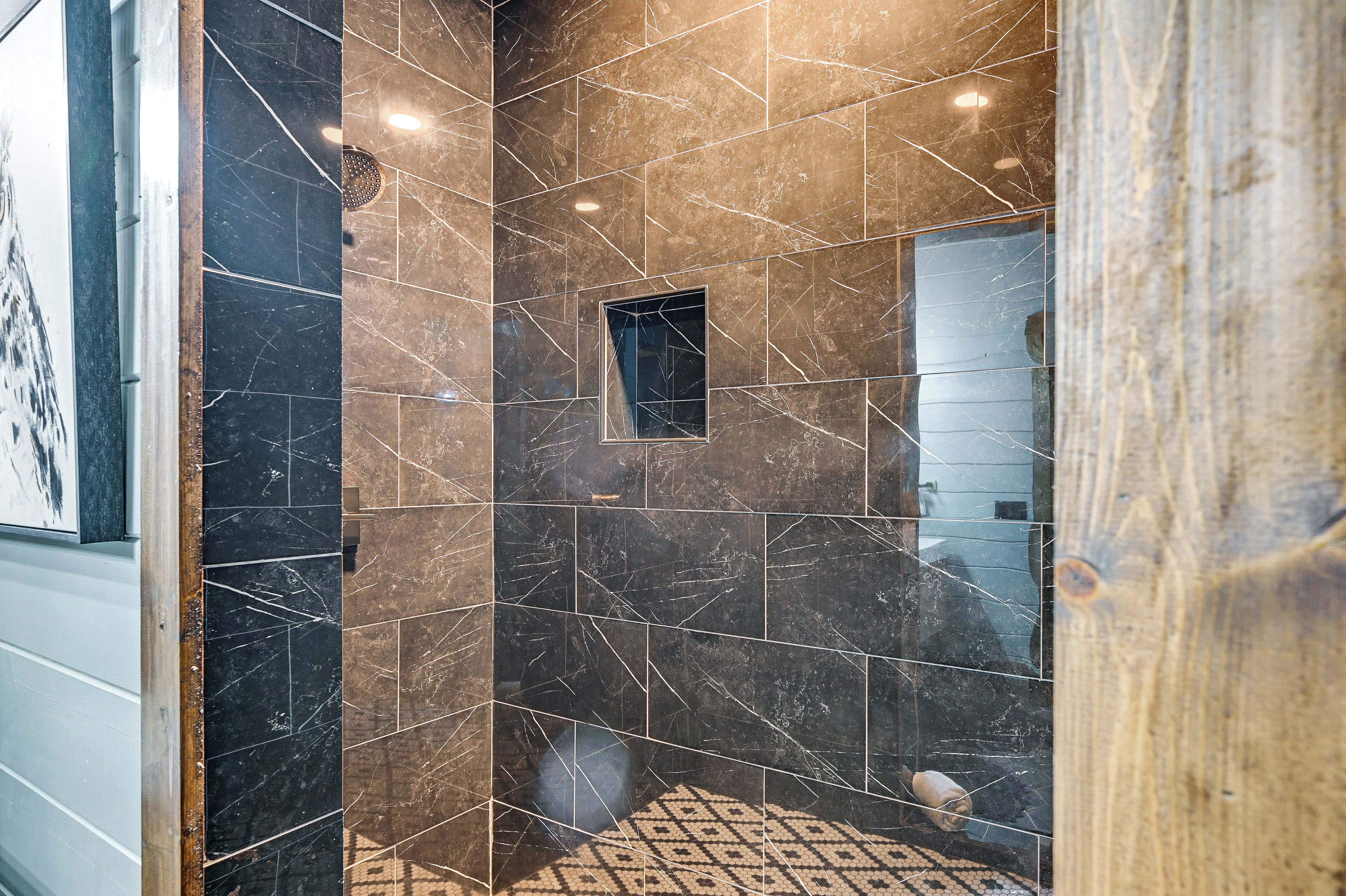 Un baño con baldosas de mármol oscuro, un ventanal pequeño y un suelo estampado.