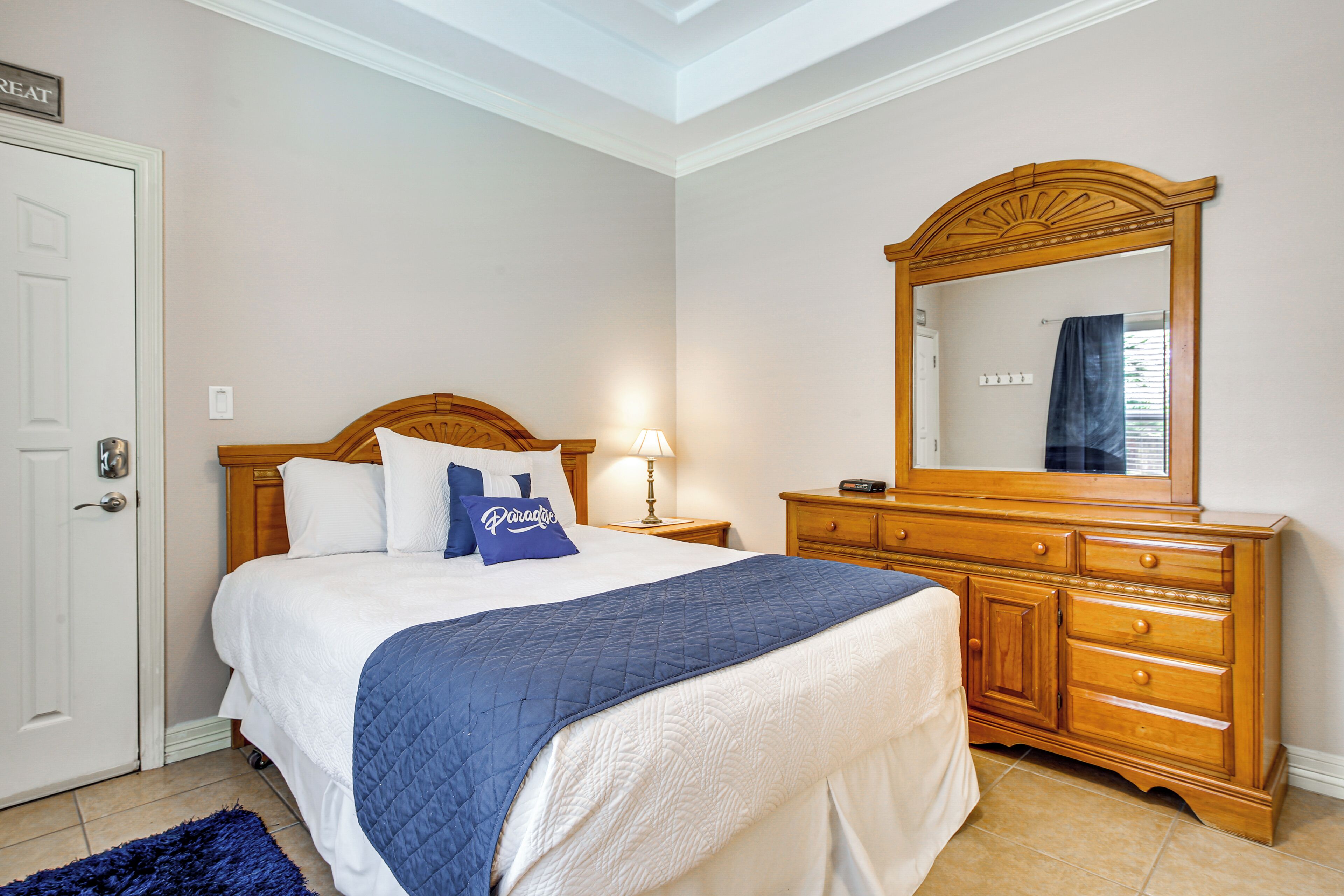 A bedroom with a bed, a dresser, a mirror, and a door.