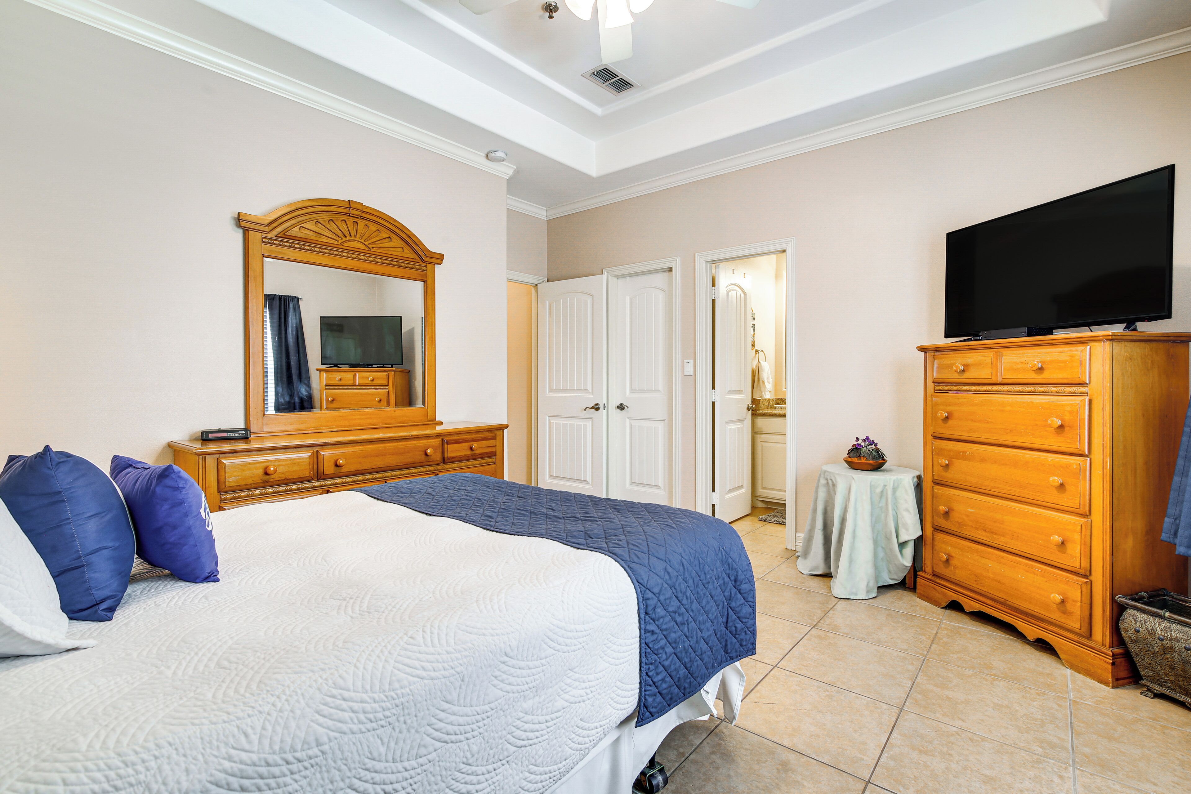 A bedroom with a bed, dresser, television, and a mirror.