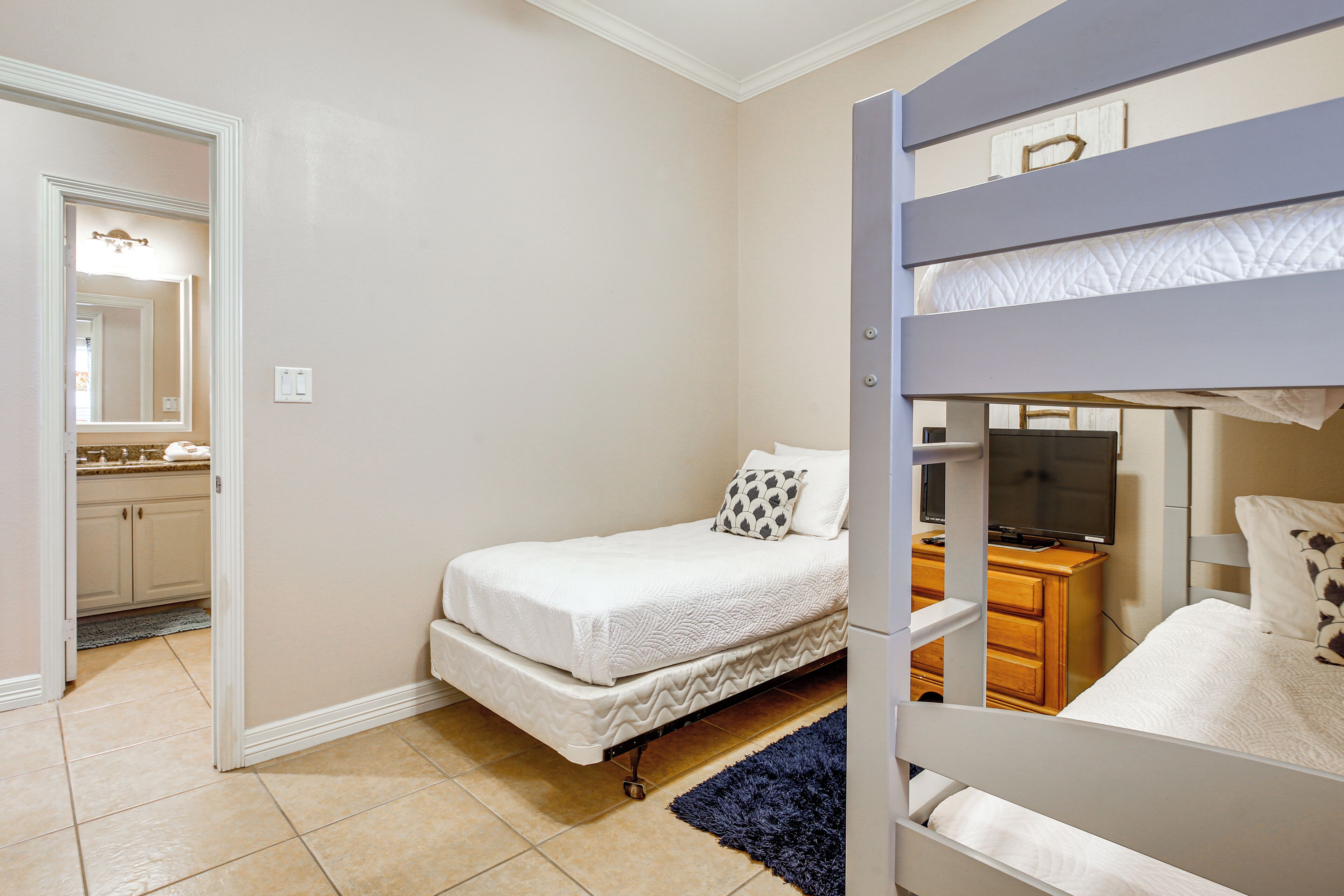 Un dormitorio con una cama individual doble, una cama sencilla, un aparador, un televisor y un baño visible a través de una puerta abierta.
