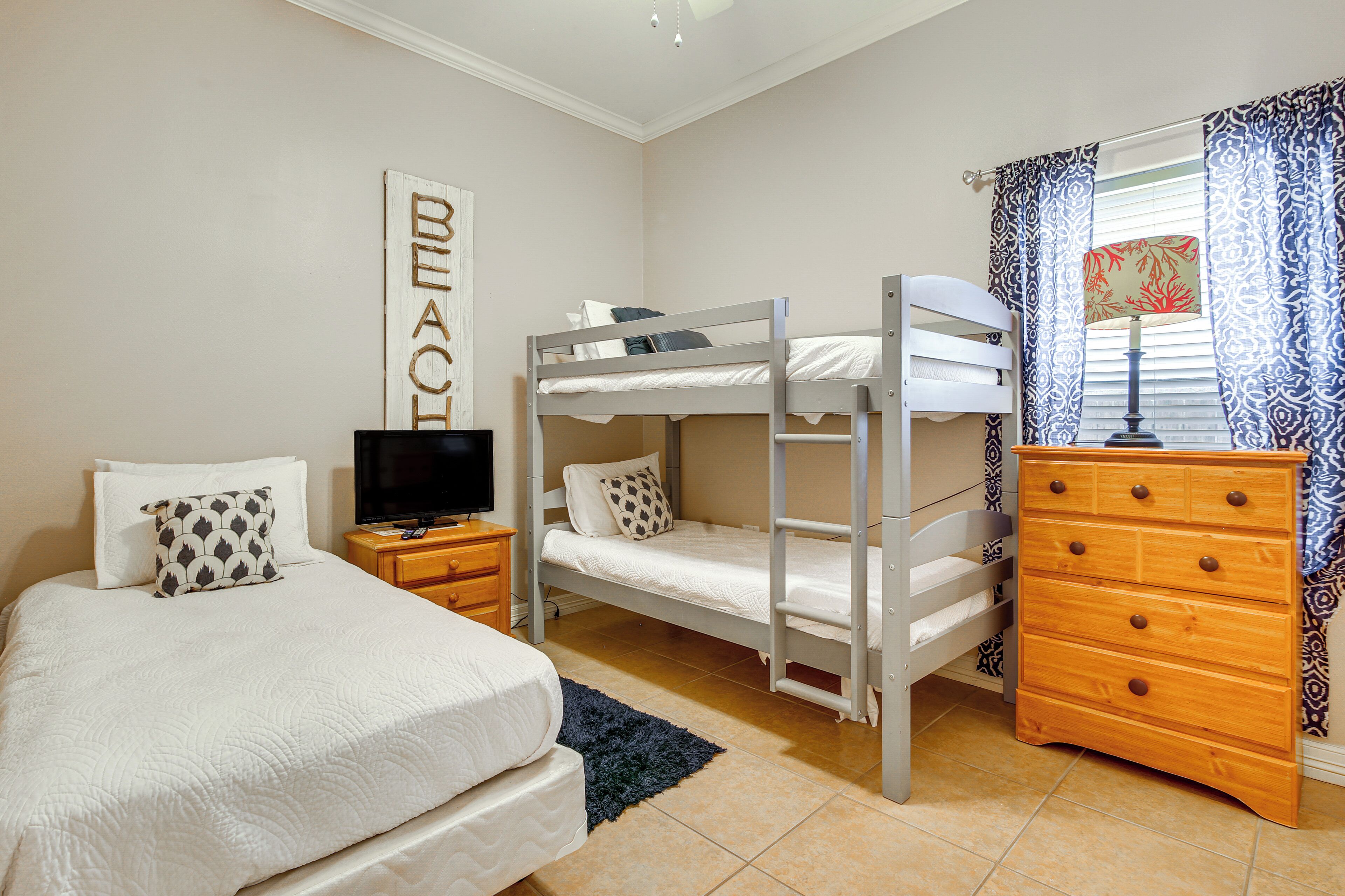A bedroom with a bunk bed, a single bed, a dresser, a television, and a wall-mounted artwork.