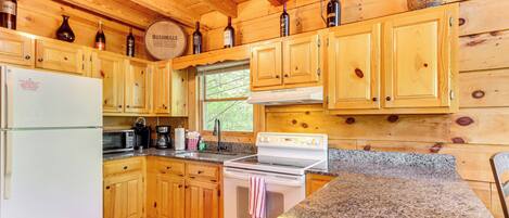 A wooden cabin kitchen with a refrigerator, stove, microwave, and wooden cabinets.