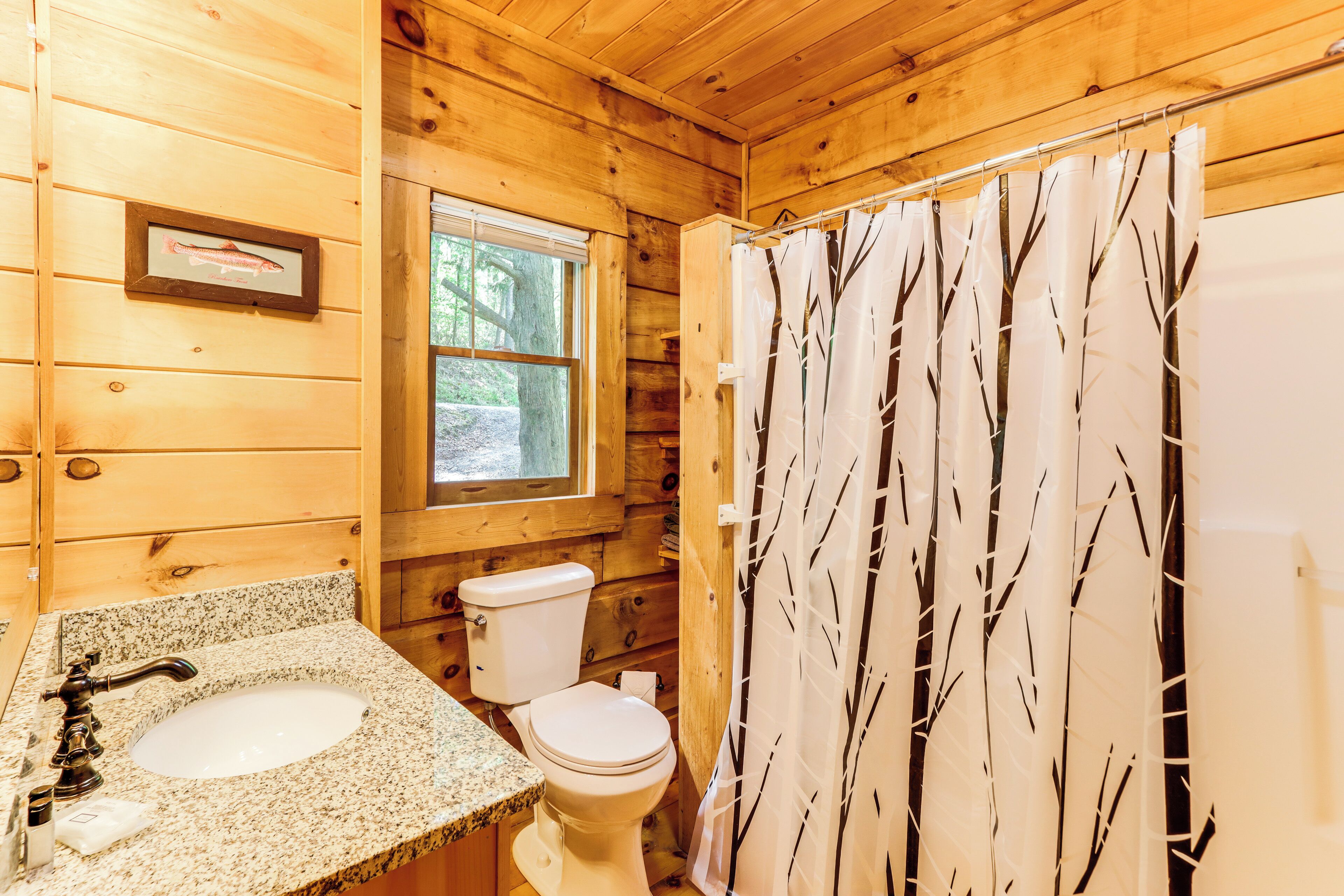 A wooden cabin bathroom with a granite sink, toilet, and a window.