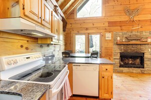 Una cocina con armarios de madera, estufa, lavavajillas y chimenea de piedra.