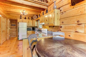 Interior de uma cabana de madeira com cozinha, incluindo uma mesa de jantar, cadeiras e armários de madeira.
