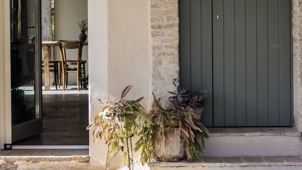 Entrada de un edificio con un arco de piedra, una puerta verde y plantas en macetas.