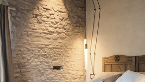 Un dormitorio con pared de piedra, una cama de madera, una mesa de metal y una lámpara colgante.