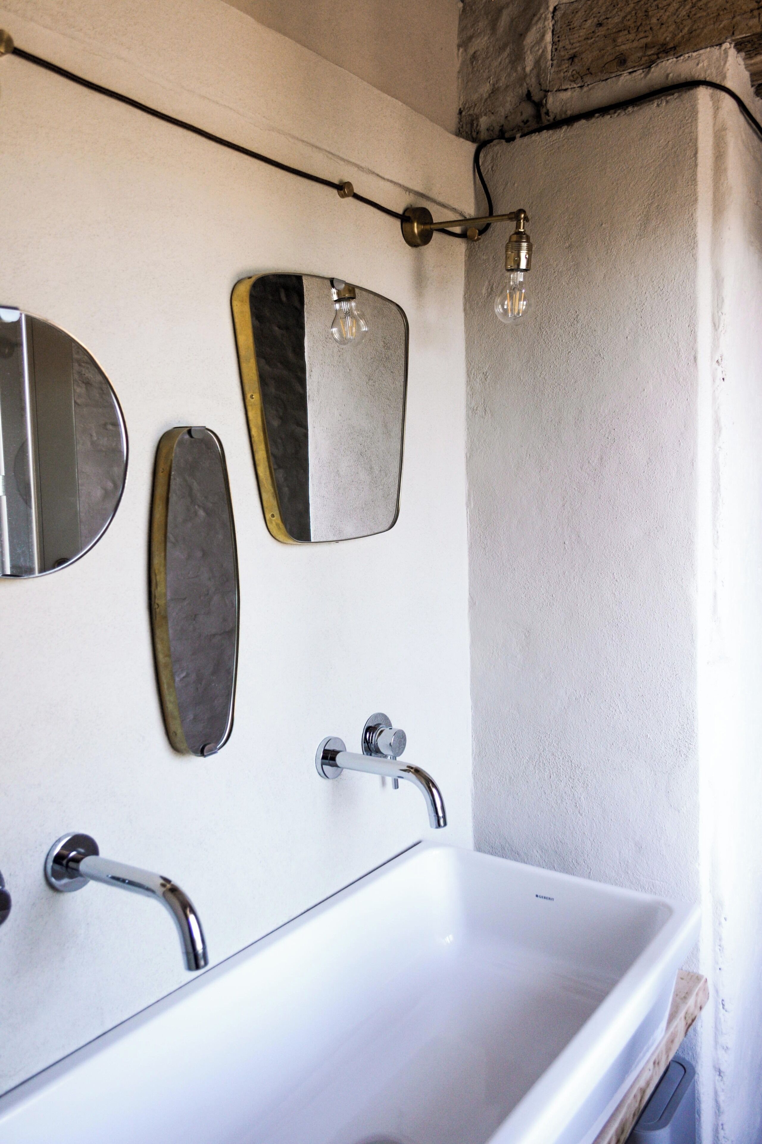 Un baño con un lavabo blanco, dos espejos y una lámpara sobre el espejo.