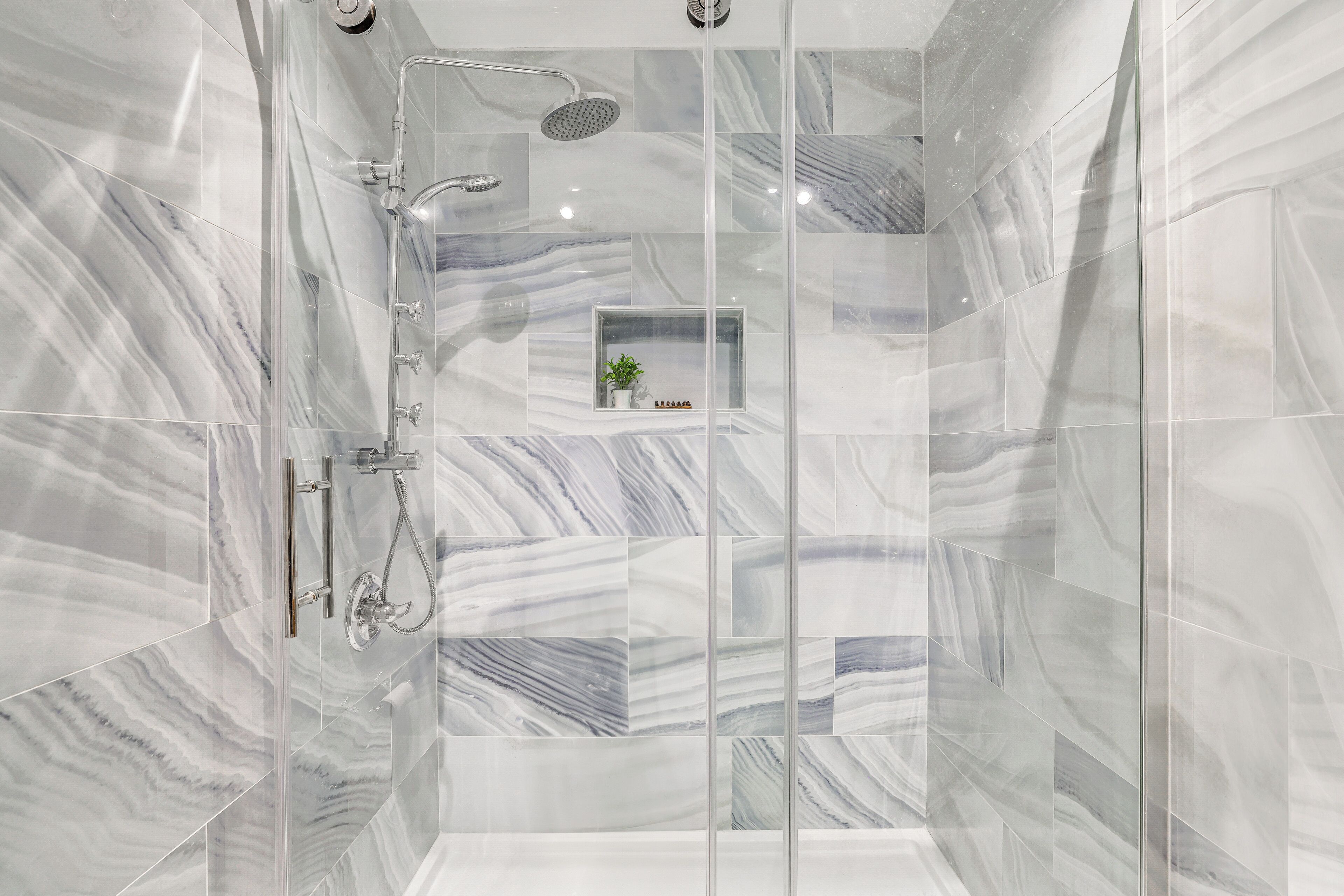 Une douche moderne avec un pare-douche en verre, des carreaux de marbre et une petite étagère sur laquelle est posée une plante.