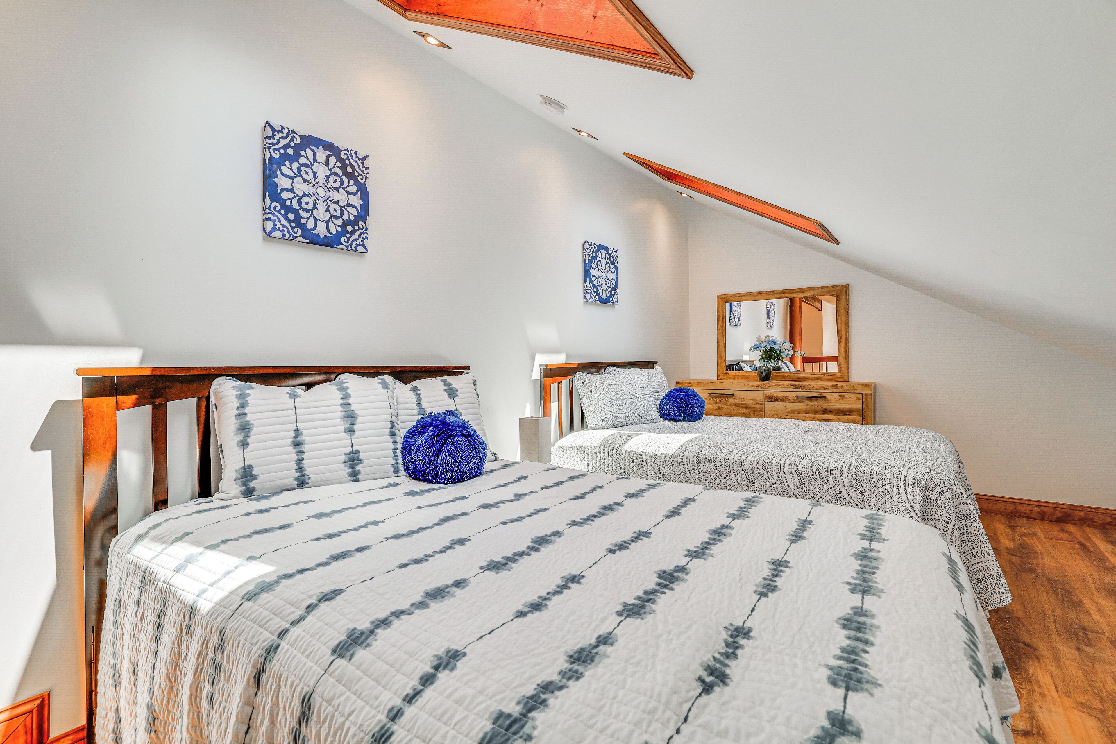 A bedroom with two beds, wooden headboards, a wooden dresser, and a sloped ceiling.