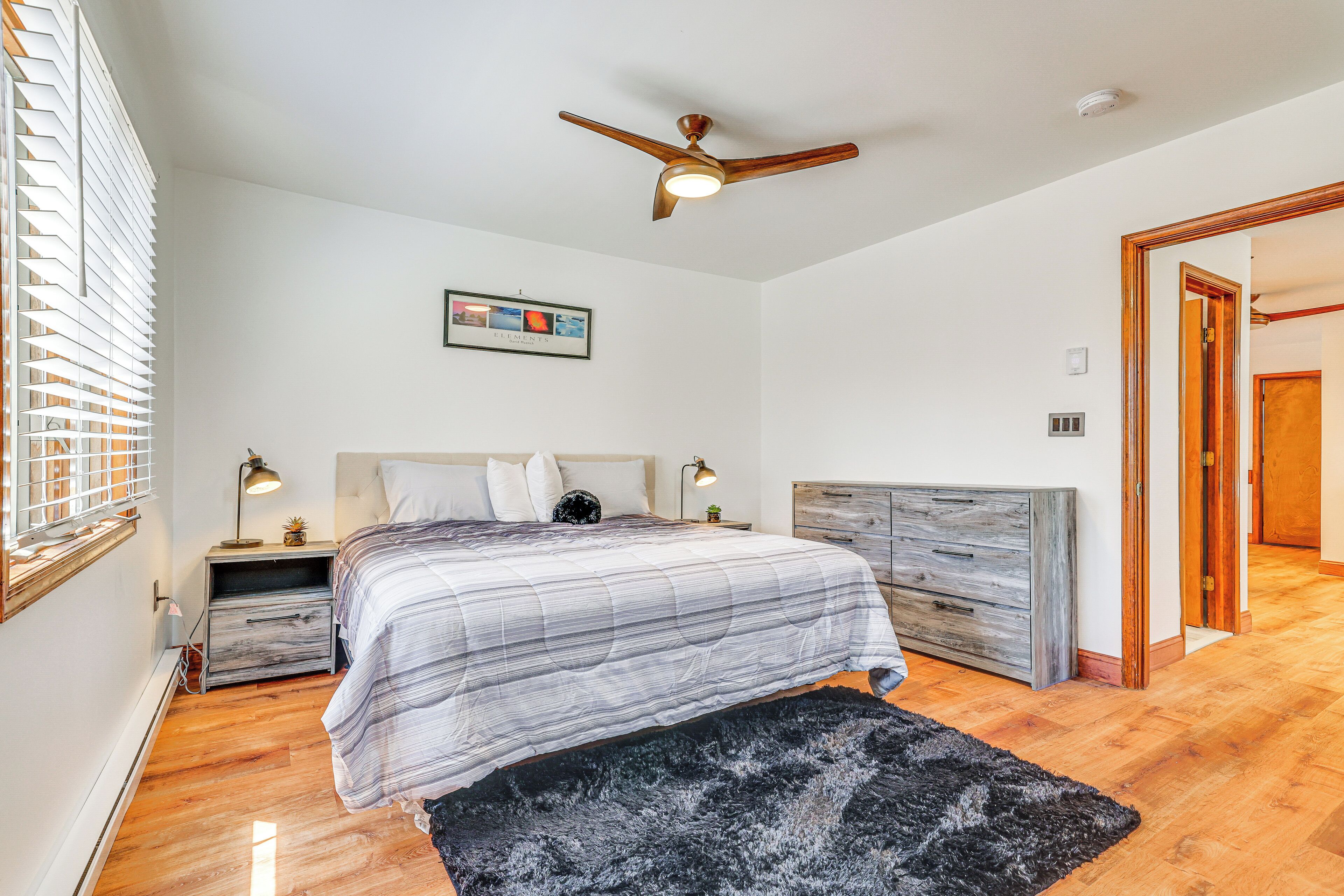 A bedroom with a bed, a ceiling fan, a nightstand, a dresser, and a framed picture on the wall.